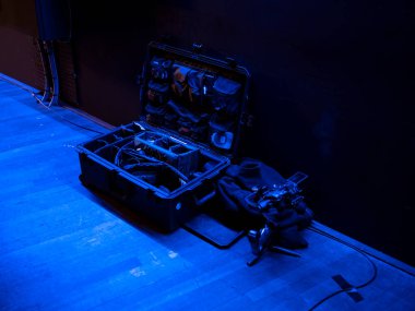 Profesyonel kamera titreşim sabitleyicide ekipman çantası sahnede atmosferik mavi ışıkta.