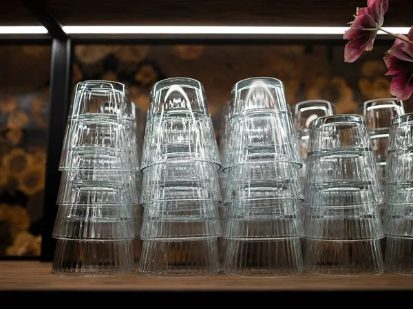 Barın rafında baş aşağı duran tırtıklı içki bardakları, çiçekli duvar kağıdı arka planı, konukseverlik iç mimarisi.