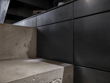 Siyah çelik mutfak dolapları, malzeme kontrastı ve işçiliğini gösteren parlak beton adımlarla buluşuyor.