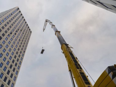 Sarı kule vinç modern binalara karşı inşaat malzemelerini kaldırıyor, ağır kaldırma operasyonunun perspektifini inceliyor