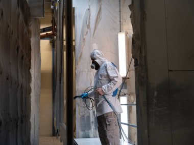 Koruyucu takım elbiseli işçiler kabin içinde sprey boya, fabrikadaki pencere ve kapı çerçevelerine bitiş palto uygulamak