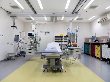 Hastanenin travma odasının kapsamlı görüntüsü hasta yatağını, izleme ekipmanlarını ve acil servis için organize tıbbi teknolojiyi gösteriyor.