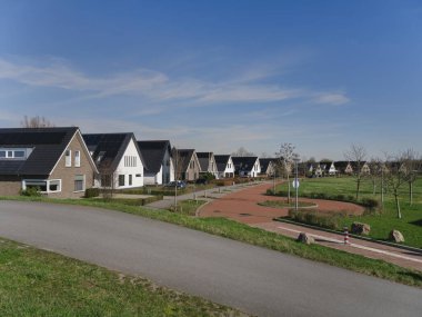 Baharda hendek üzerinde kırmızı tuğla bisiklet yolu boyunca güneş panelleri olan modern Hollandalı aile evleri.