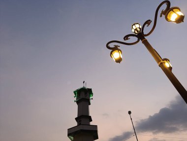 Illuminated streetlight glows warmly against a serene dusk sky, with a building tower silhouetted in the background, creating a peaceful urban scene perfect for travel and cityscape visuals.
