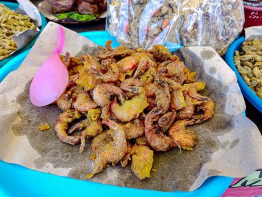 Golden fried shrimp piled high on parchment paper on a bright blue tray presents an appetizing snack at a market food stall, perfect for travel and cuisine advertising.