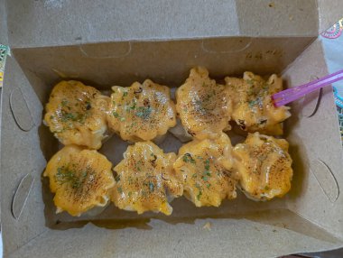 Steamed dumplings are topped with creamy orange sauce and herbs in a cardboard box, presenting a tasty and appealing image for food blogs and restaurant menus.
