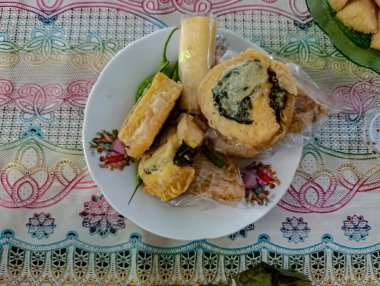 Assorted golden fried foods and green chili peppers are displayed on a white floral plate, placed on a vibrant patterned tablecloth, suggesting a colorful and appetizing meal for food-related content.