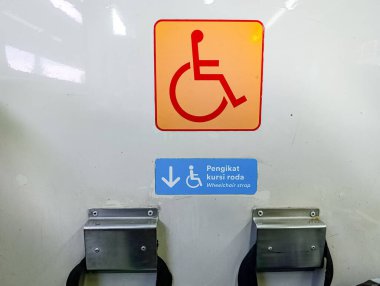 Accessibility sign showing wheelchair access, in orange and red on a white wall, suggests inclusivity and assistance for individuals with mobility challenges, ideal for public service announcements and accessibility awareness campaigns.