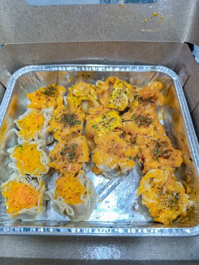 Delicious shumai dumplings topped with vibrant orange sauce sit in a silver tray, offering a close-up view with bright lighting, perfect for food blogs and restaurant promotions.