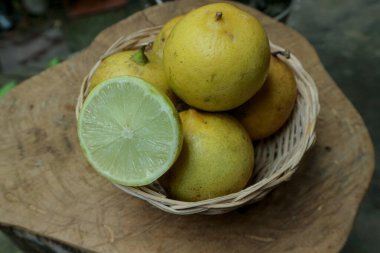 Birkaç sarı limon ahşap bir yüzeyde bir sepete konur, limonun yarısı içini gösterir, doğal ve organik bir his yaratır, mutfak malzemeleri için mükemmeldir..