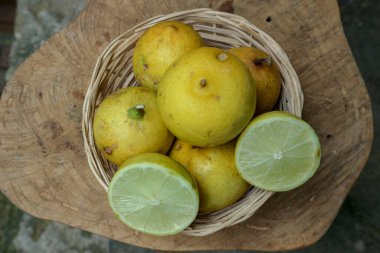 Yıpranmış ahşap bir yüzey üzerinde dokuma sepetine yerleştirilmiş taze, olgun limonlardan oluşan genel çekim; yenilenen ve doğal bir görüntü yemek ya da yiyecek projeleri için harika.