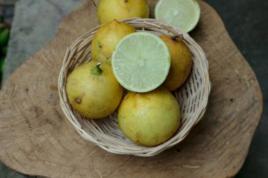 Köhne ahşap bir yüzeyde dokuma sepetine yerleştirilmiş taze limonlar, yiyecek ve içecek promosyonları için ideal doğal ve sağlıklı bir titreşim sunar..
