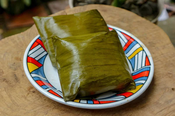 İki yeşil ambalajlı yiyecek, ahşap bir yüzey üzerinde renkli bir tabakta duruyor. Uluslararası mutfak ve yemek sunumu için mükemmel..