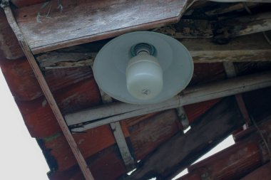 Beyaz bir ampul, eski ahşap bir tavanı kırmızımsı-kahverengi fayanslarla aydınlatarak, eski ve yıpranmış bir estetik yaratarak ev yapımı ve mimari stok tasvirleri için uygun hale getiriyor..