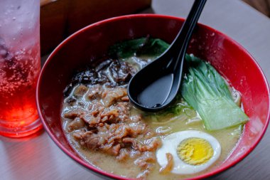 Lezzetli ramen kasesi kırmızı bir kasenin yanında yumurta, et ve yeşillik içeriyor. Lezzetli ve davetkar bir sunum yaratıyor. Yemek temalı reklamlar için mükemmel..