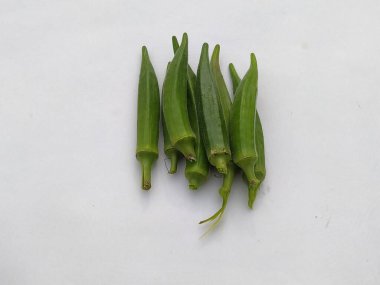 Bir yığın taze yeşil bamya kabuğu, bembeyaz bir zemine karşı sergileniyor. Tarifleri ve sağlıklı beslenmeyi betimlemek için ideal..