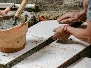 İnşaat ortamında havan ve aletlerle seramik fayanslar döşeyen bir işçinin elleri, modern iç tasarım için temiz ve hassas bir yüzey yaratıyor, inşa ve yenileme için ideal..