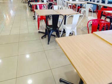 Açık bej döşemeleri, modern siyah beyaz kırmızı sandalyeleri ve ahşap masaları olan boş bir kafeterya yemek yemek ve sosyalleşmek için ideal bir ortam yaratıyor..