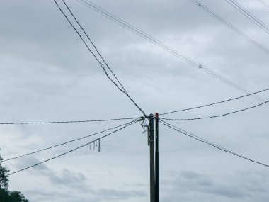 Bulutlu gri gökyüzüne uzanan çoklu elektrik hatlarına sahip elektrik direği altyapı ve hizmet temaları için uygun minimalist bir sanayi sahnesi oluşturuyor.