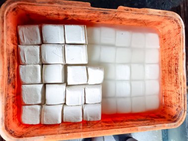Su dolu turuncu plastik bir kabın içinde düzgünce dizilmiş bir yığın beyaz tofu küpü yiyecek ve mutfak pazarlaması için uygun taze ve temiz bir görünüm yaratıyor..