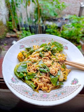 Bahçedeki çiçekli bir tabakta yeşil sebzeli ve çubuklu erişte tabağı canlı, doğal ve yemek ve yaşam tarzı pazarlaması için ideal bir ortam yaratır..