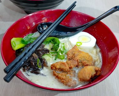 Kızarmış tavuk parçaları, haşlanmış yumurta, yeşil soğan ve koyu mantarlı Asya ramen çorbasıyla dolu canlı kırmızı bir kase yemek severler ve restoran pazarlama için mükemmel bir lezzet ve cazip atmosfer yaratıyor..