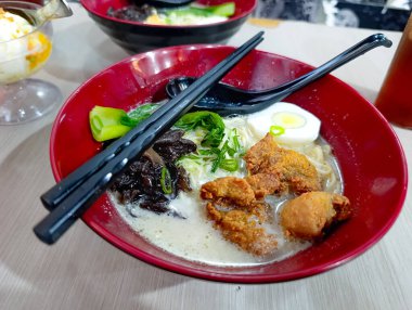 Kızarmış tavuk, yeşil soğan, kaynamış yumurta ve siyah çubuklu siyah et suyu içeren canlı bir kase rahat ve davetkar bir atmosfer yaratıyor. Günlük yemek ve yemek tutkunları için mükemmel..