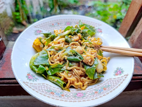 Açık havada doğal ışıklandırmayla dekoratif bir tabakta servis edilen yeşil yapraklı, yumurta parçaları ve soslu taze şehriye tabağı yemek sunumu ve günlük yemek pazarlaması için mükemmel sıcak, davetkar bir atmosfer yaratıyor..