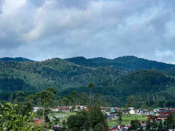 Yoğun yeşil ormanlar ve bulutlu gökyüzü altında evleri olan küçük bir köyün bulunduğu manzaralı dağ manzarası seyahat ve doğa temaları için mükemmel barışçıl ve doğal bir atmosfer yaratıyor..
