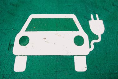 Yeşil yüzeyi şarj eden beyaz elektrikli araba simgesi. EV şarj bölgeleri, sürdürülebilir hareketlilik ve modern ulaşım altyapısı için net işaretleme. Ekoloji, enerji ve kentsel hareketlilik temaları için ideal.