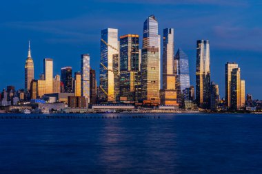 New York şehri alacakaranlıkta parlıyor. Hudson Nehri şehrin ikonik gökdelenlerinin parlak ışıklarını yansıtıyor..