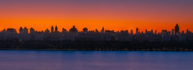 New York şehri alacakaranlık üzerine çöktüğünde binalarda parıldayan ışıklarla canlı bir günbatımının altında parlıyor..