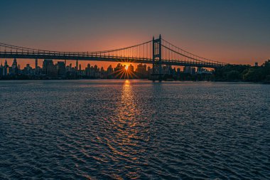 Güneş Triborough Köprüsü 'nün arkasında batıyor. New York şehrinin ufuk çizgisine ve Doğu Nehri' ne altın bir parıltı saçıyor..