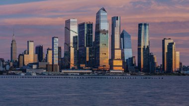 New York şehri gökyüzü ve binaların canlı renklerini yansıtan Hudson Nehri ile gün batımında gökyüzü parlar..