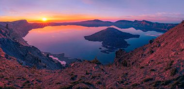Büyücü Adası 'nın Gündoğumu Serenity Krater Gölü Ulusal Parkı' ndaki panoramik krater gölü manzaralı bir güneş doğumu sunuyor. Volkanik bir kül konisi olan ada gölün çarpıcı güzelliğine katkıda bulunur..