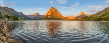 Montana 'daki Buzul Ulusal Parkı' nda gün doğumunda Grinnell Point, Swiftcurrent Gölü 'nde aynalar. 1915 'te inşa edilen tarihi Many Buzul Oteli ve Wilbur Dağı manzarada da görülebilir..