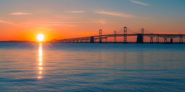 Sandy Point, Maryland 'den Chesapeake Körfezi Köprüsü' nde gün doğumu, güneşin suyun üzerinde parıldayan yansımasıyla köprünün siluetini, şafağın canlı renklerine karşı sergiliyor. William Preston Yolu J