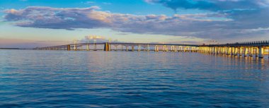 Bay Bridge Sunset Serenity: Chesapeake Körfezi Köprüsü olarak da bilinen William Preston Lane Jr. Memorial Bay Köprüsü, Maryland 'in doğu ve batı sahillerini birbirine bağlayan Chesapeake Körfezi boyunca uzanır. Görüntü, günbatımının sıcak ışığını yansıtır.