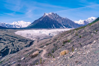 Sarmal bir patika, kayalık bir moraine boyunca uzanır. Uçsuz bucaksız buz sahasına ve Blackburn Dağı 'nın karla kaplı zirvelerine doğru..