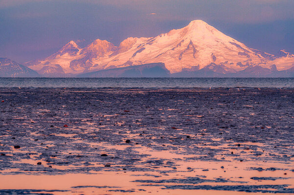 Вулкан Иллиамна величественно стоит над спокойным морем на закате, с приливом, открывающим скалистый берег..