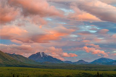 Denali 'nin zirvesi, bulutlar gökyüzünde sürüklenirken batan güneşle aydınlanır..