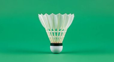 A close-up studio shot of a white badminton shuttlecock with its feathers spread, set against a plain green backdrop.