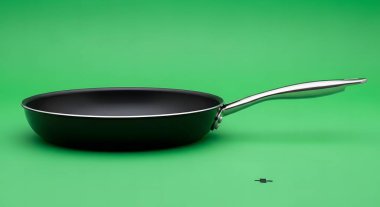 A close-up studio shot of a non-stick frying pan with a sleek metal handle, isolated on a solid green backdrop.