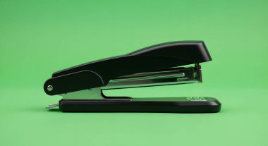 A black stapler is shown in profile against a solid green background, highlighting its design and function as an office tool.