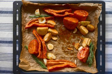 Domates, biber, sarımsak ve biberiye fırınlanmaya hazır bir çarşaf üzerindeki parşömen kağıdında. Sıcak sonbahar mutfak sahnesi, mevsimlik aşçılık için mükemmel..