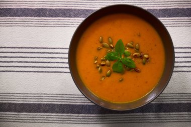 Balkabağı tohumu ve taze fesleğenle süslenmiş siyah bir kasede kremalı balkabağı çorbası. Sıcak sonbahar yemeği, mevsimlik yemek ve sağlıklı yemek için mükemmel..
