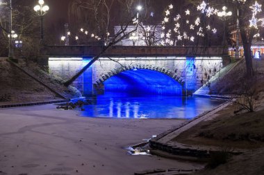 Riga 'daki Bastion Hill şehir parkında (Letonya) Alexander Köprüsü' nün gece manzarası. Köprü 1858-1859 yılları arasında inşa edildi ve 1902 yılında genişletildi..