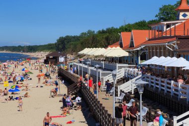 ZELENOGRADSK, KALINGRAD REGION, RUSSIA - 18 Haziran 2019: Baltık Denizi kıyısındaki ünlü tatil beldesi Zelenogradsk 'ta (eski adıyla Cranz), ahşap restoran yakınlarındaki kumlu bir sahilde dinlenen bilinmeyen insanlar