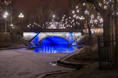 Riga 'daki Bastion Hill şehir parkında (Letonya) Alexander Köprüsü' nün gece manzarası. Köprü 1858-1859 yılları arasında inşa edildi ve 1902 yılında genişletildi..