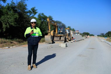 Gün doğumunda yeni bir yol projesi üzerinde yürüyen inşaat denetçisi, altyapı gelişimi ve gelecekteki ilerlemeyi sembolize ediyor.